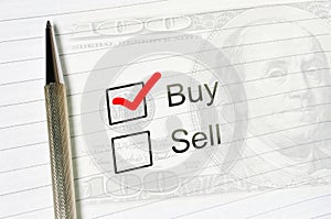 Buy choice or sell, marked check box with a pen on lined paper dollar background. Trade concept