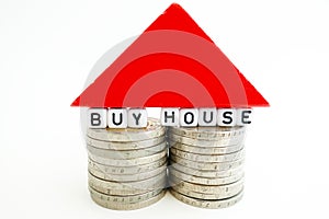 â€œBuy houseâ€ text on two piles of coins with red wooden piece forming a small house