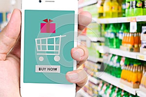 Buy now on smart phone screen in hand with blurred supermarket b