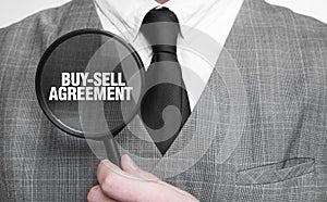 BUY-SELL AGREEMENT words on magnifying glass and businessman