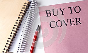 BUY TO COVER text on pink paper with notebooks