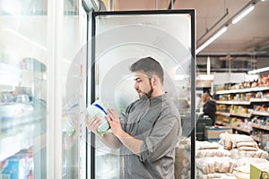 Buyer breaks the refrigerator door in the supermarket, holds the package in his hands and looks at the label. Man chooses frozen