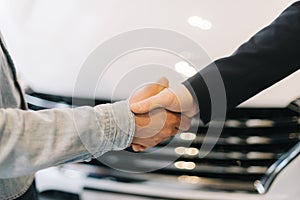 Buyer of car shaking hands with seller in auto dealership, in front of car