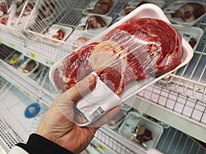 Buyer hand with beef meat packageat the grocery store. Close up of man holding wrapped meat in grocery store