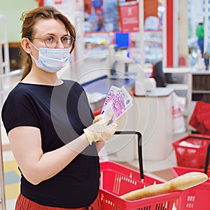 A buyer in a medical mask recounts money euros at the supermarket checkout