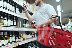 A buyer with a red wine basket chooses wine in the alcohol store of the store. The choice of goods in the supermarket.