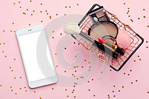 Buying beauty products online concept. Shopping basket with makeup cosmetics and mobile phone with blank white screen mockup on