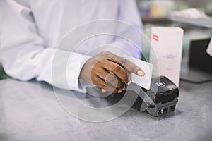Buying with credit card in the pharmacy. Cropped image of hands of African woman pharmacist swiping credit card of