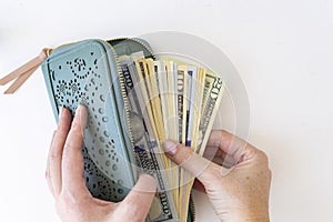 Buying for dollars. A woman`s hand holds a green wallet and counts out money. White background