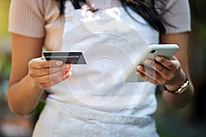 Buying extra, an owners optimism. a young business owner using a cellphone and credit card at work.