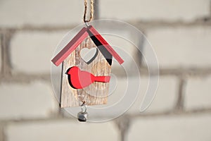 Buying house concept. Wooden Christmas toy house with red roof and bird on white brick wall. Christmas decoration