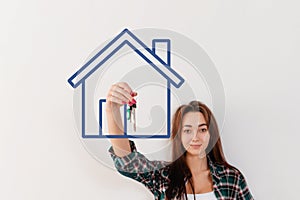 Buying and renting real estate. A woman in a plaid shirt holds a bunch of keys, in a painted blue house. Hand in focus