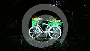 Bycicle decorated with fairy christmas lights isolated at black night with beautiful flowers and plants in the basket