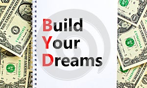 BYD build your dreams symbol. Concept words BYD build your dreams on white note on a beautiful background from dollar bills.