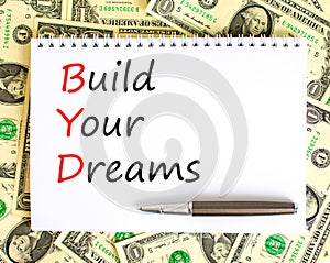 BYD build your dreams symbol. Concept words BYD build your dreams on white note on a beautiful background from dollar bills. Pen.