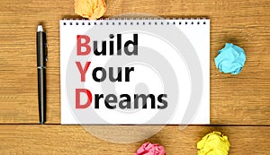 BYD build your dreams symbol. Concept words BYD build your dreams on white note on a beautiful wooden table wooden background. Pen