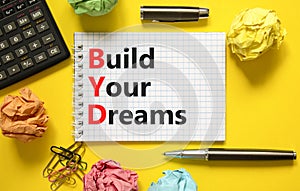 BYD build your dreams symbol. Concept words BYD build your dreams on white note on a beautiful yellow background. Black pen.