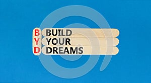 BYD build your dreams symbol. Concept words BYD build your dreams on wooden stick on a beautiful blue table blue background.