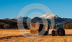 A mountain rises above a tractor and hay field