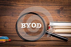 Byod concept. Magnifying glass with text on wooden office table