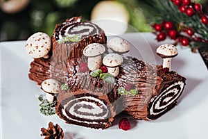 BÃ»che de NoÃ«l with merengue mushrooms and mint leaves on top of chocolate glazing.