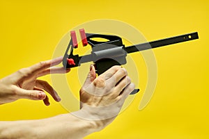 C-clamp in male hands isolated on yellow background