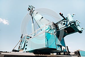 A cab with the operator of a Large blue car crane that stands ready to operate on hydraulic supports on a platform next to a large
