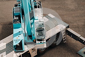 A cab with the operator of a Large blue car crane that stands ready to operate on hydraulic supports on a platform next to a large