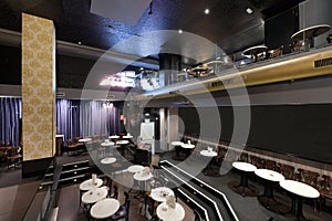 Cabaret theater type venue with two heights and round white tables with black chairs