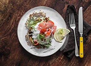 Cabbage fritters with smoked salmon and greek yogurt sauce on a wooden background, top view. Delicious breakfast, tapas,