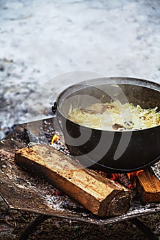 Cabbage with meat cooking in a cauldron on open fire