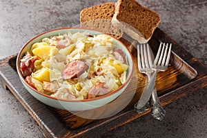 Cabbage stewed with potatoes, sausage, bacon and onions close-up in a bowl. Horizontal