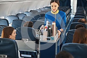 Cabin attendant leading trolley cart through plane aisle