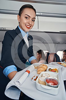 Cabin attendant smiling while going with airline catering trolley