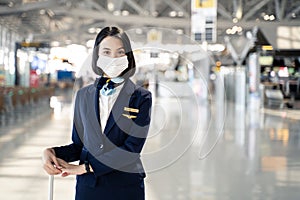 Cabin crew or air hostess wearing face mask walking in airport terminal to the airplanel during the COVID pandemic to prevent coro