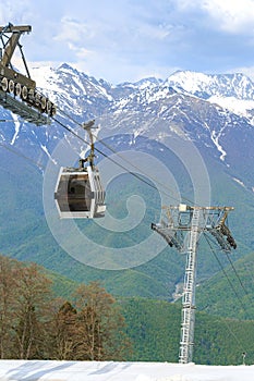 Cabin of the funicular above a snowy ski track against the backdrop of green forests and mountains