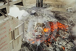 Cabin of overhead crane with mechanical multivalve clamshell grapple on a background evaporation of molten liquid red-hot iron and