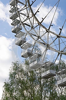 Cabins of Ferris wheel against a cloudy sky. Near a birch tree. Spring day in the park.