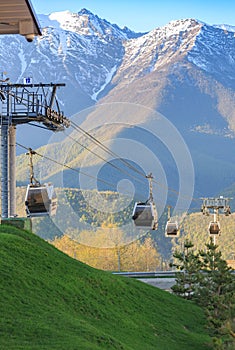 Cabins of funicular on the background of green grass and snow-capped mountains