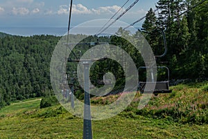 Cable car empty seats among trees, grass field in green forest on hill, sunny summer blue sky with white clounds, baikal lake