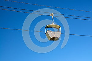 Cable car on rope of cableway, blue clear sky background in sunny summer day