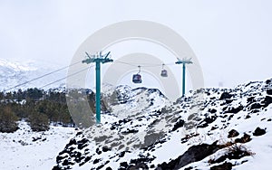 Cable car to Mount Etna national park in winter. View of volcanic terrain with black volcanic lava stones and snow under