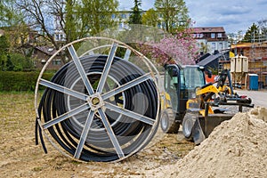Cable for electric power supply on wooden spool on a construction site. Small yellow excavator