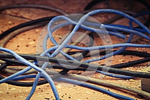 Cable power cords in a tangled mess on floor of workplace, used dirty electric outlet