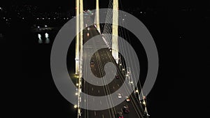 A cable-stayed highway bridge with tall concrete pylons illuminated by architectural lighting at night. Orbital