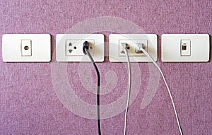 Cables plugged in a white electric outlet mounted on pink wall