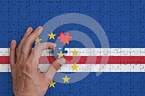 Cabo verde flag is depicted on a puzzle, which the man`s hand completes to fold