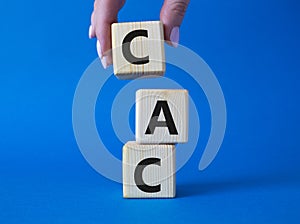 CAC - Customer Acquisition Cost symbol. Wooden cubes with word CAC. Beautiful blue background. Businessman hand. Business and
