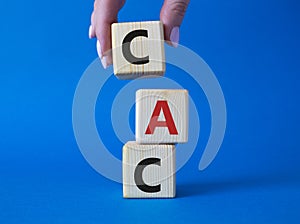 CAC - Customer Acquisition Cost symbol. Wooden cubes with word CAC. Beautiful blue background. Businessman hand. Business and