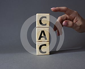 CAC - Customer Acquisition Cost symbol. Wooden cubes with word CAC. Beautiful grey background. Businessman hand. Business and